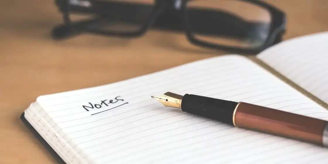 Libreta abierta con una pluma y unas gafas encima de una mesa